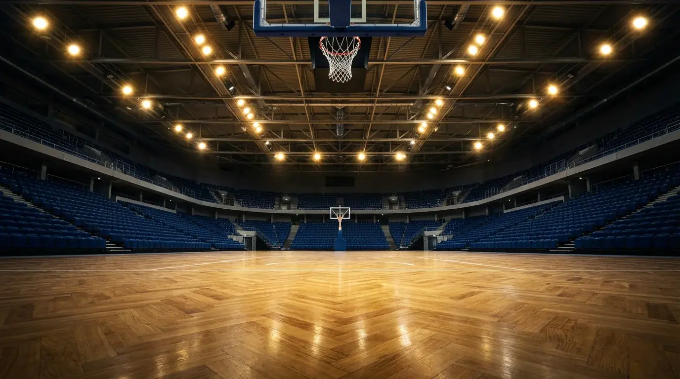 Pabellón de baloncesto europeo moderno con gradas iluminadas y pista de parqué vacía antes del salto inicial